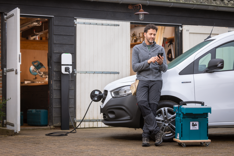 Een vakman leunt op zijn elektrische wagen en kijkt op zijn smartphone
