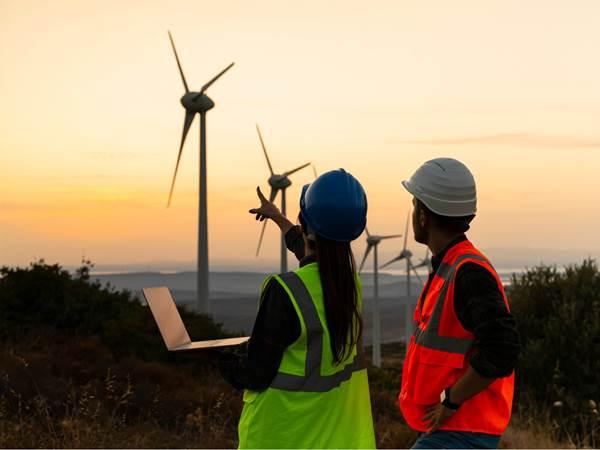 Mechanics point towards wind turbines during sunset