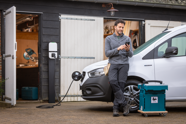 Un artisan consulte son smartphone pendant que sa voiture électrique se recharge