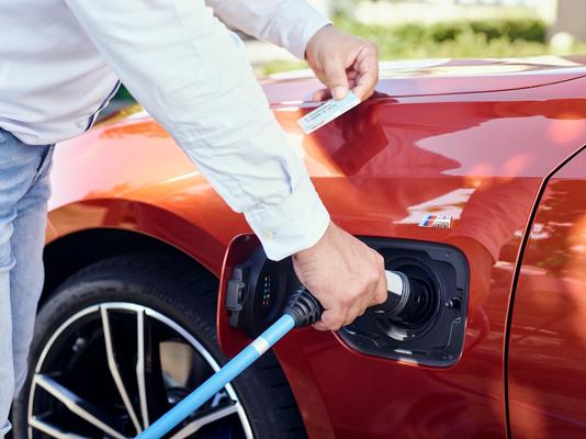 Een persoon stopt de stekker van de laadpaal in de auto