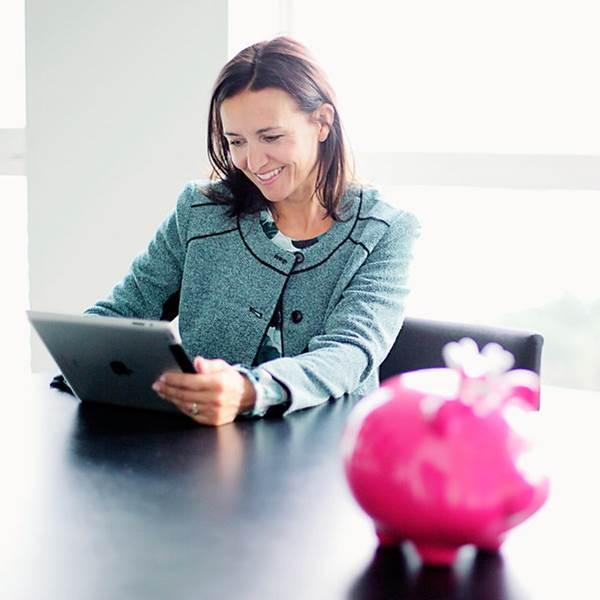 Vrouw kijkt naar tablet met een roze spaarvarken op het bureau