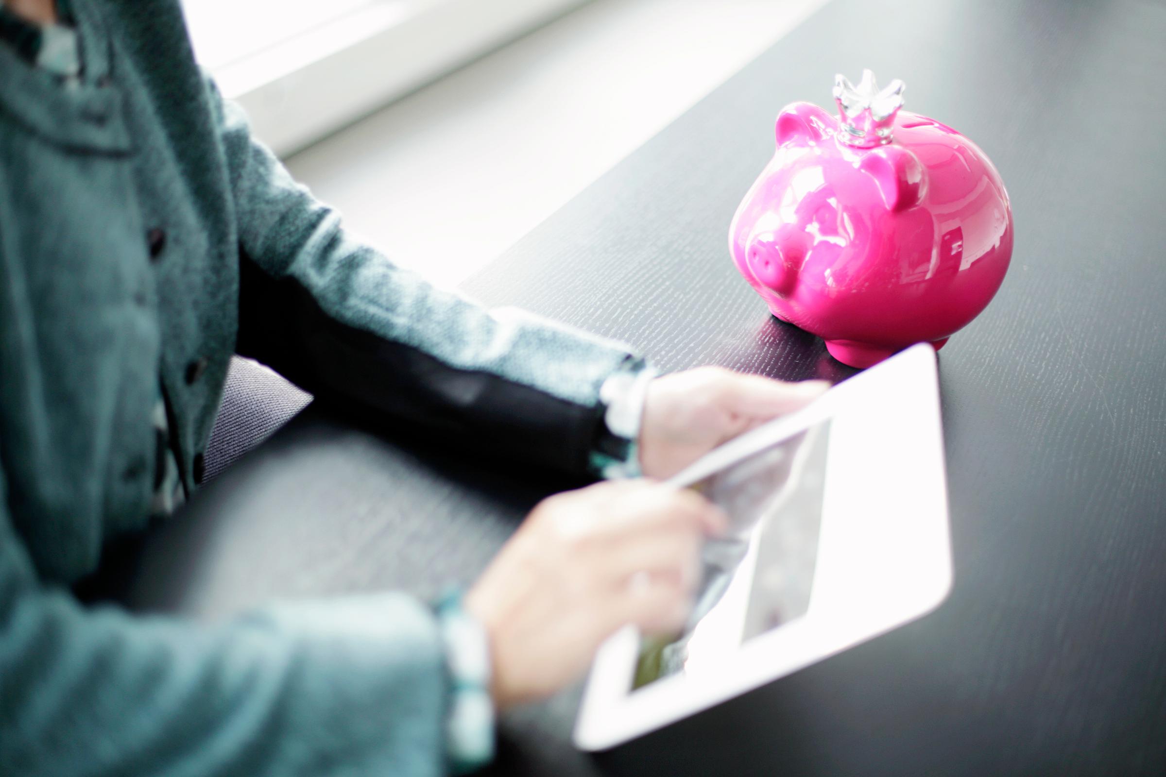 Quelqu'un travaille sur une tablette, près d'une tirelire.