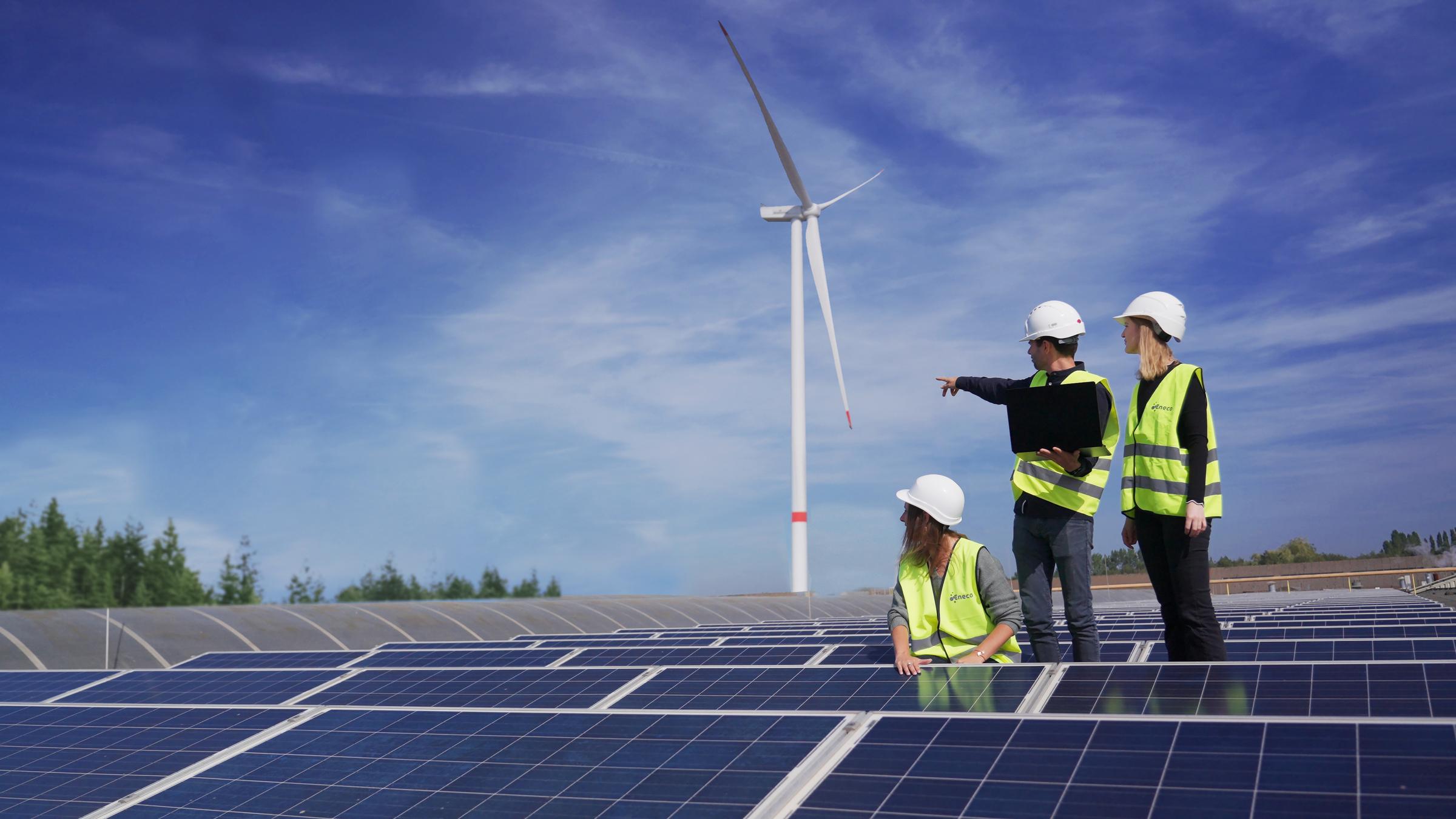 Een team Eneco-techniekers bekijken een windmolen en zonnepaneleninstallatie