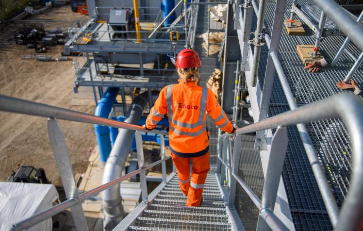 Technicien Eneco en équipement de sécurité orange descendant un escalier métallique sur un chantier industriel