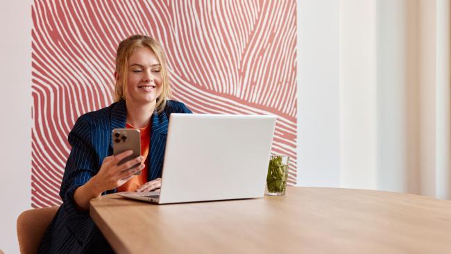 Vrouw zit aan bureau kijken naar haar latop en telefoon