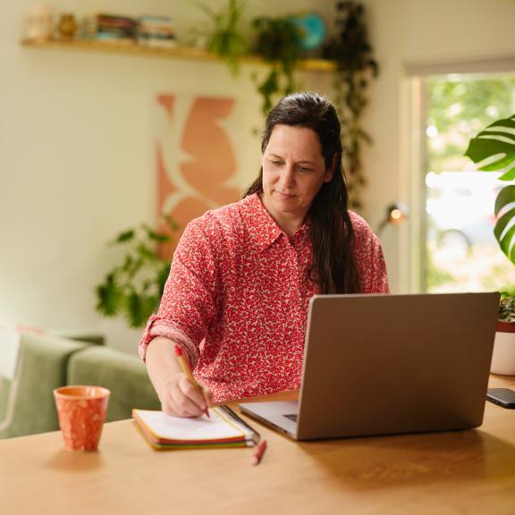 Vrouw werkt op laptop en schrijft iets op