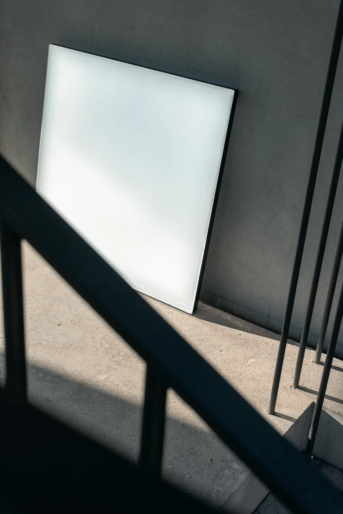 Il pannello LED Light Fields III è appoggiato a una parete di cemento su un pianerottolo e riflette la luce diurna diffusa in un ambiente moderno.