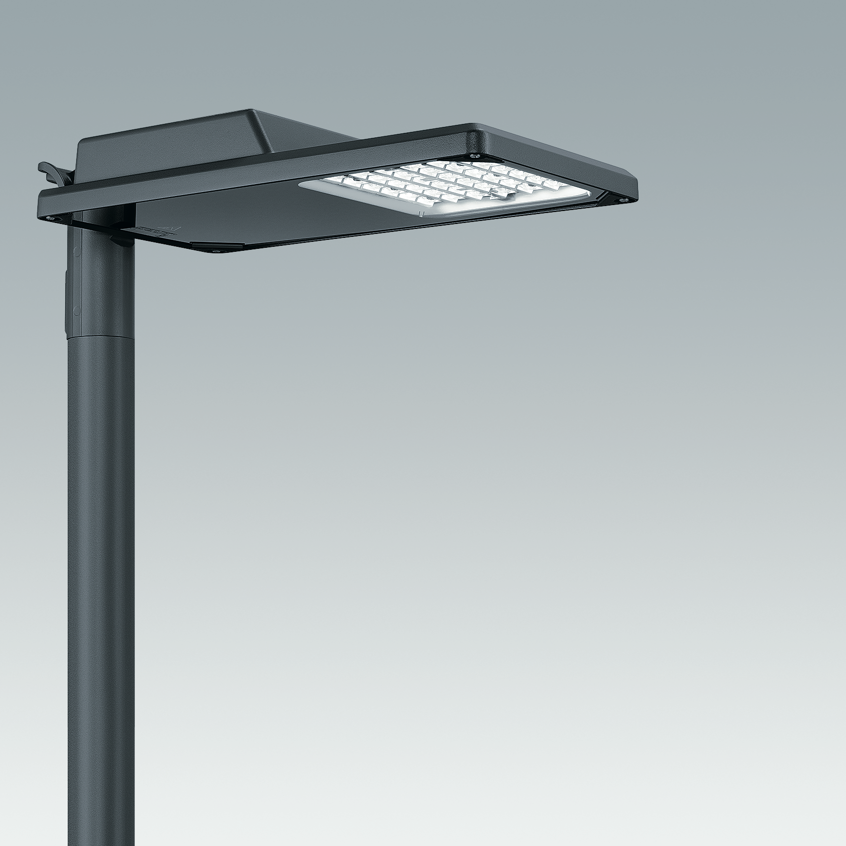Moderno lampione a LED con corpo piatto e rettangolare montato su un palo scuro. La luce è accesa, illuminando l'area sottostante con un bagliore bianco freddo.