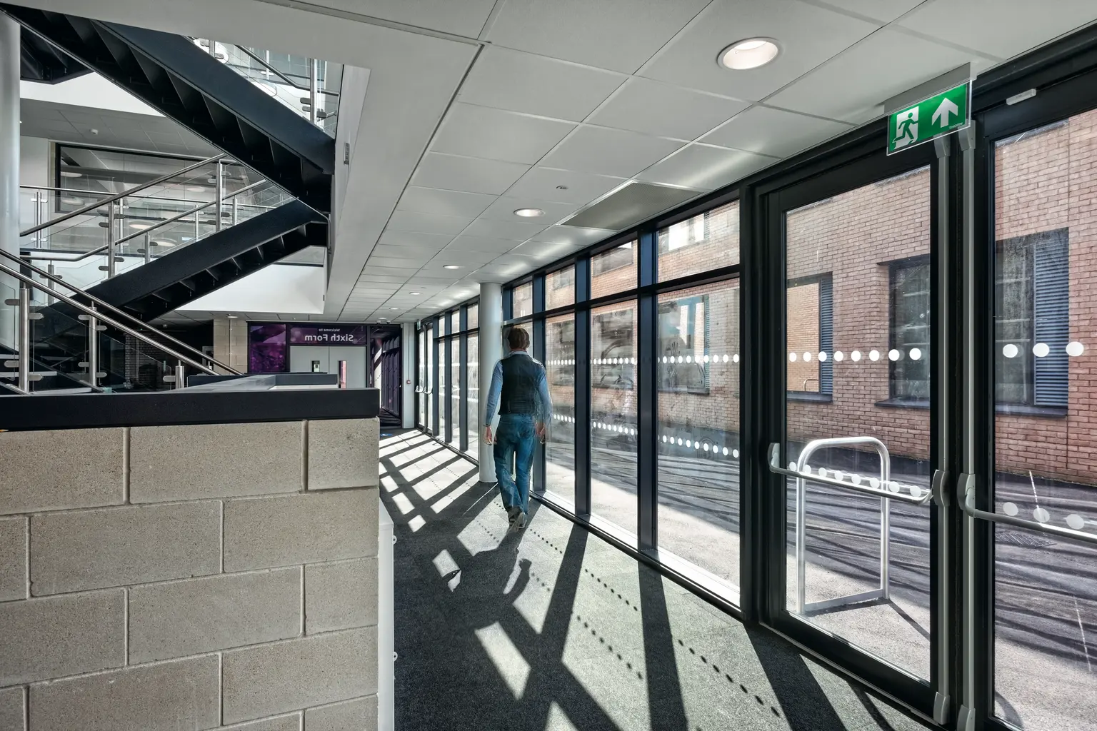 Heller Flur mit großen Glasfenstern, die natürliches Licht hereinlassen, ergänzt durch Deckeneinbauleuchten für gleichmäßige Beleuchtung. Mit modernen architektonischen Elementen, einschließlich einer Treppe und polierten Oberflächen.