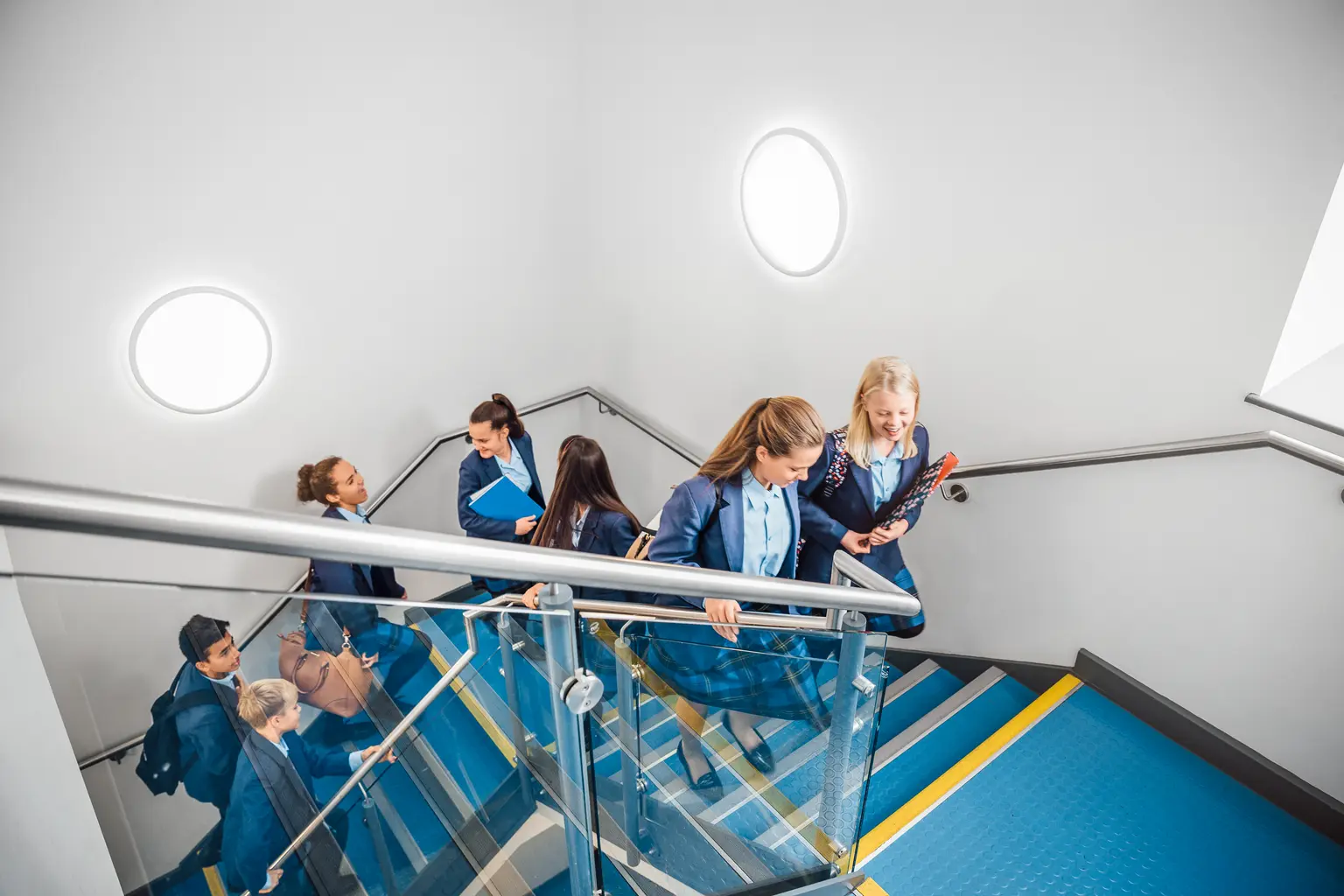 Ein Schulkorridor mit blauen Stufen, durch den Kinder gehen, während der Bereich mit Wandleuchten von Thorn beleuchtet wird