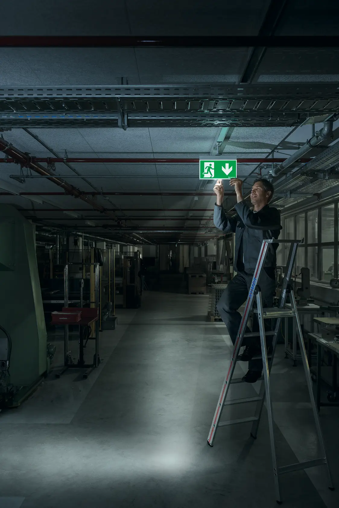 Ein Techniker installiert das CROSSIGN Beleuchtungssystem an der Decke in einem industriellen Lager, das warmweißes Licht gleichmäßig ausstrahlt.