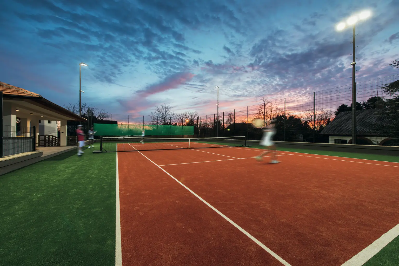 Un campo da tennis con un giocatore che serve la palla durante una partita serale