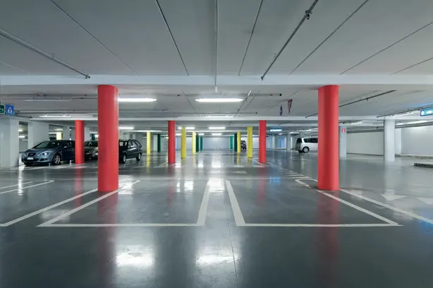 A modern parking garage equipped with new LED luminaires from Zumtobel. In the middle, two red columns can be seen.