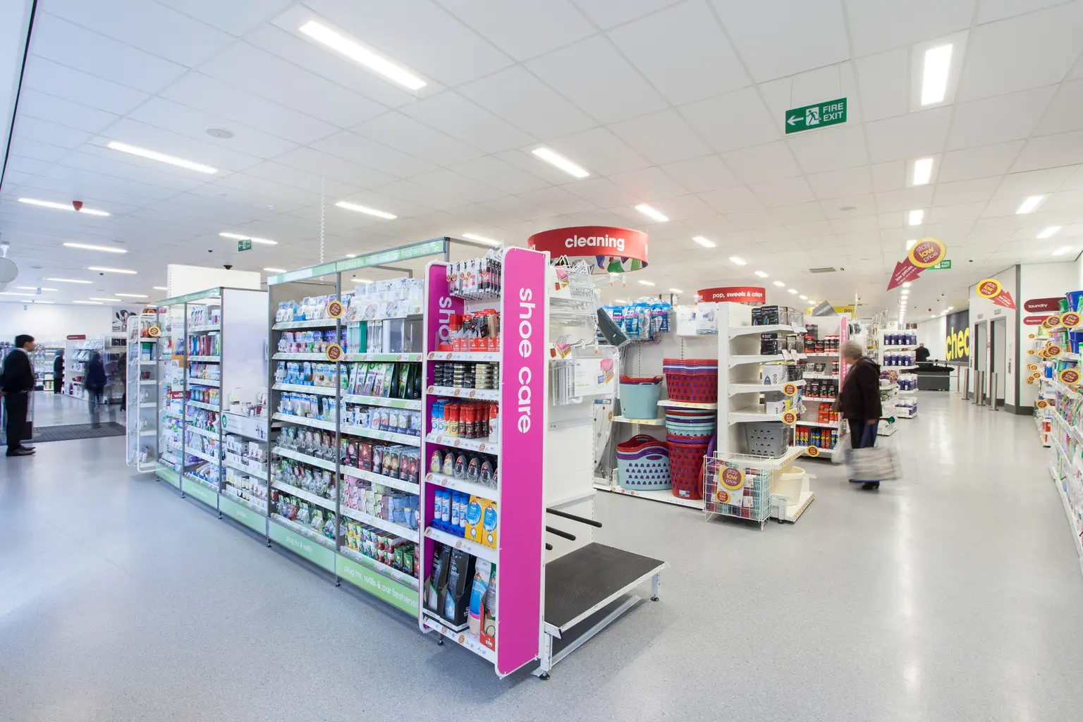 Un corridoio di un supermercato ben illuminato con scaffali pieni di prodotti per la pulizia e articoli per la casa. La pubblicità luminosa sopra le sezioni, come "pulizia", aiuta a organizzare lo spazio, mentre la disposizione aperta consente una facile navigazione.