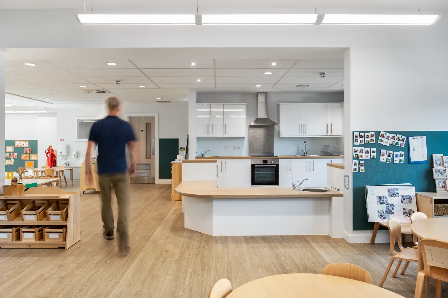 Una cucina moderna per l’asilo nido e un’area giochi con pavimenti in legno caldi, illuminazione brillante e un design aperto, che favorisce uno spazio di apprendimento accogliente e funzionale.