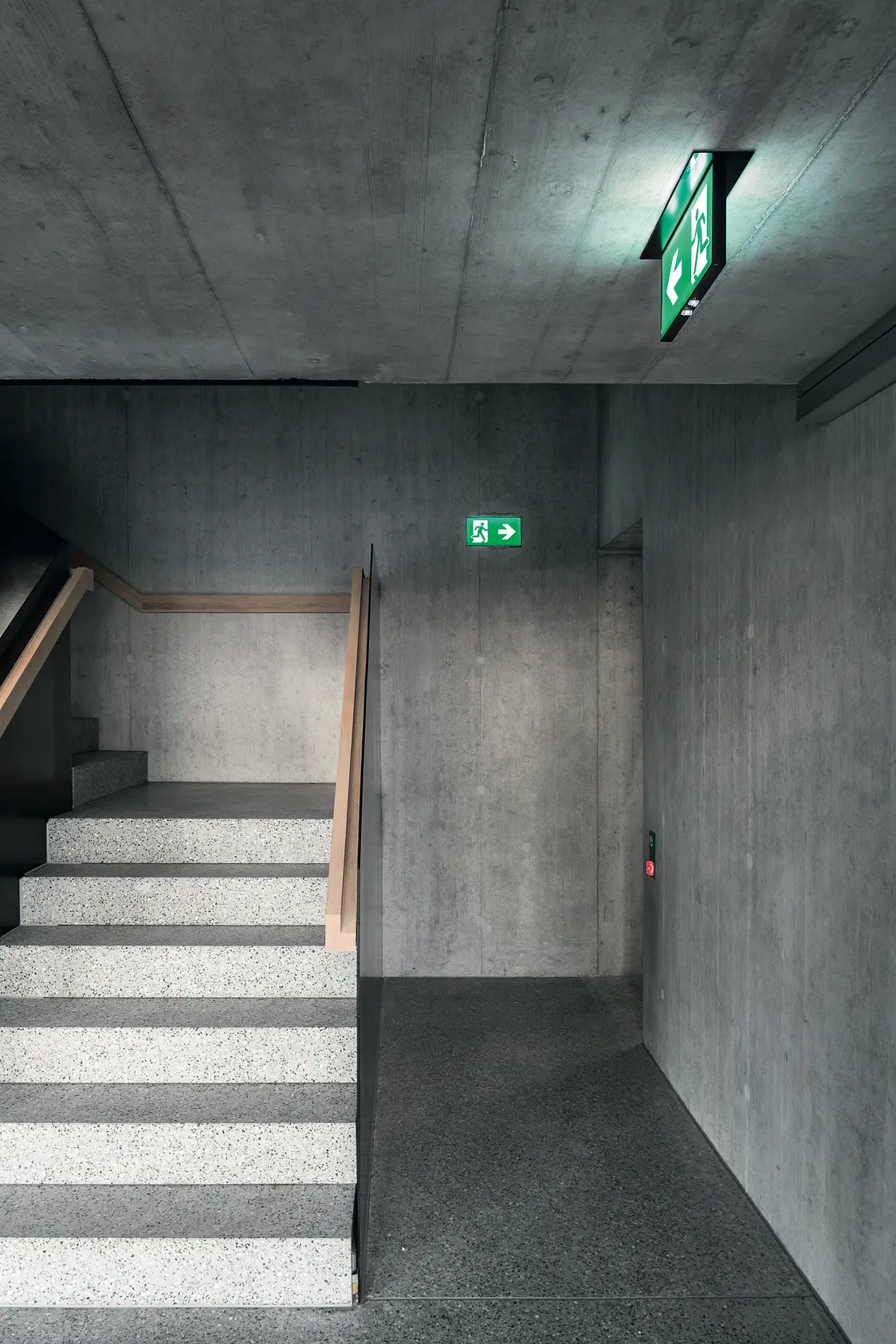 La luce di emergenza PURESIGN in una moderna scala in cemento inserita in un vano scale minimalista.
