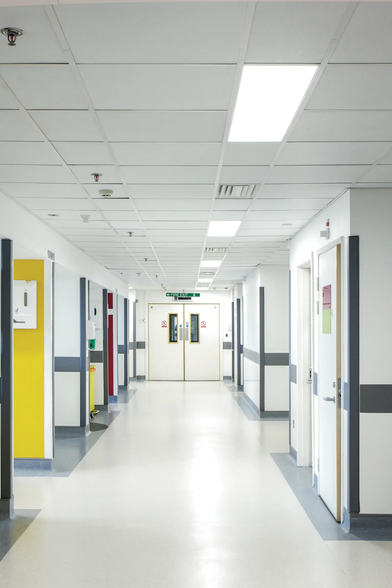 Corridoio ospedaliero luminoso con pavimenti lucidi, pareti bianche e pannelli LED a soffitto.