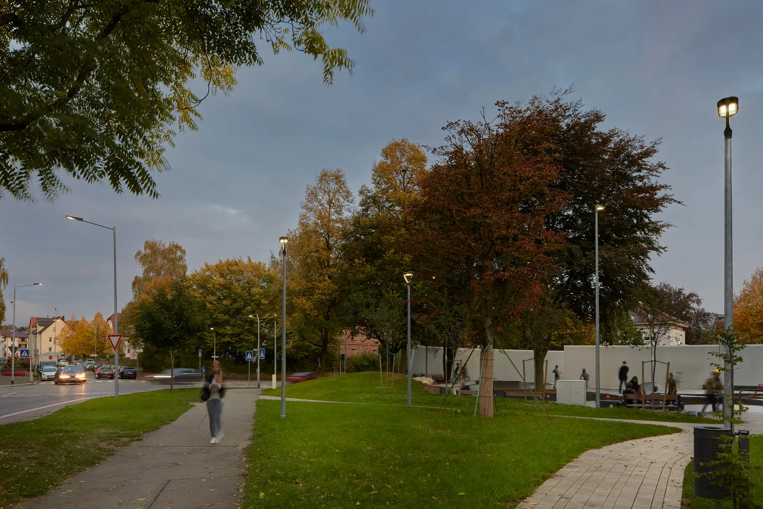 Ein Weg und eine Grünfläche neben einer Straße sind gleichmäßig beleuchtet, sodass sie von Fußgängern und Radfahrern auch nach Einbruch der Dunkelheit komfortabel genutzt werden können.