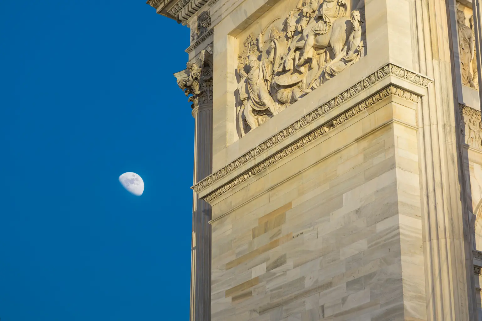 Un primo piano dell'Arco della Pace mostra dettagliate sculture in pietra, con la luna che brilla sullo sfondo.