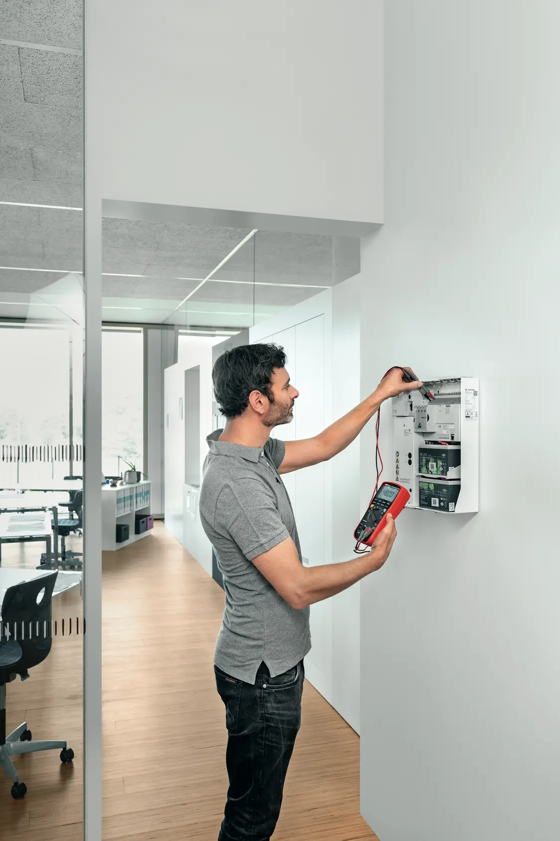  Ein Techniker testet das Beleuchtungssystem ONLITE central nBOX in einem modernen Büro mit Glaswänden und Holzboden auf Funktionalität.