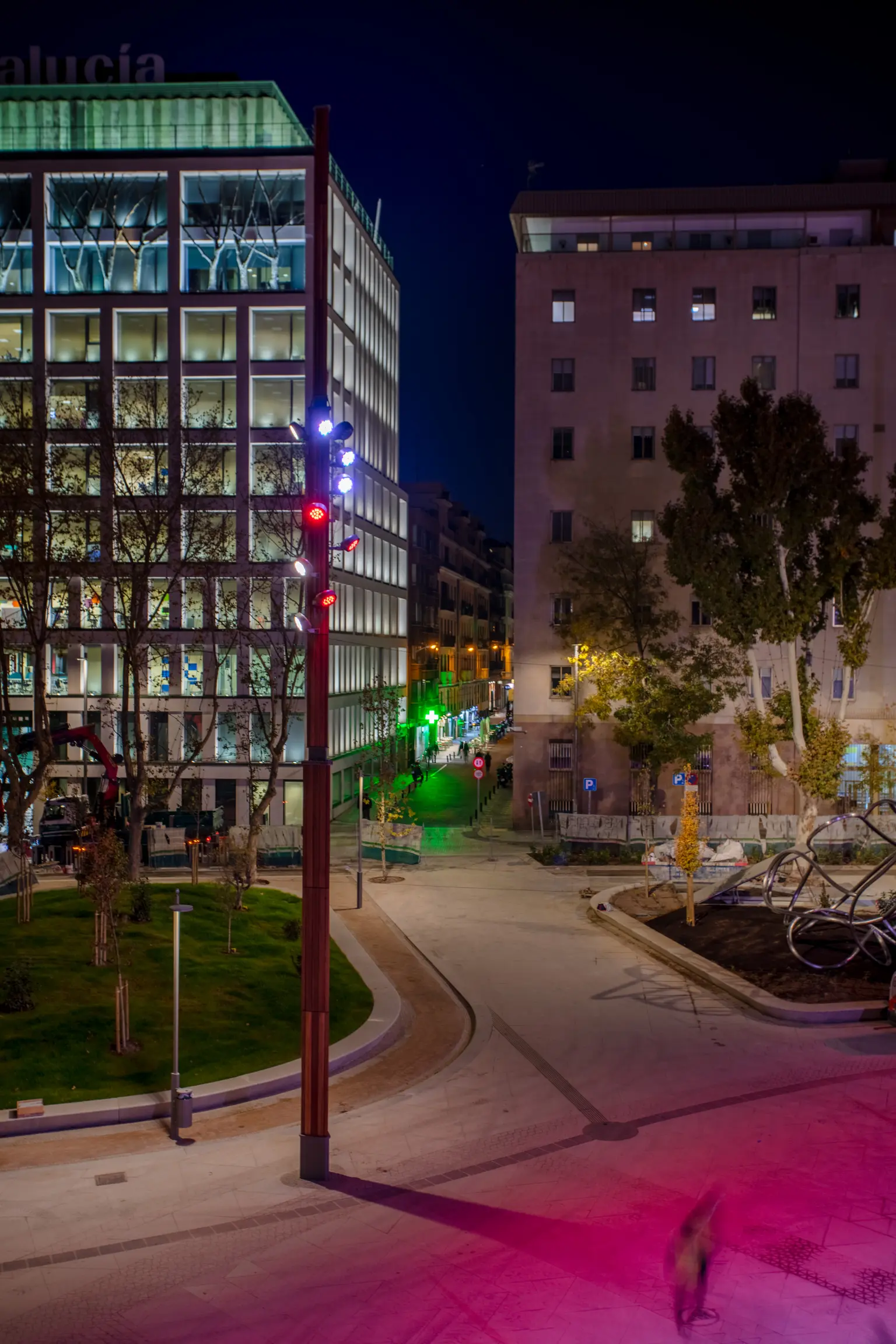 La combinazione di illuminazione rossa e bianca sul palo crea effetti visivi sorprendenti, mentre le proiezioni di luce colorata sul terreno contribuiscono a un'atmosfera vivace e accogliente nello spazio pubblico.