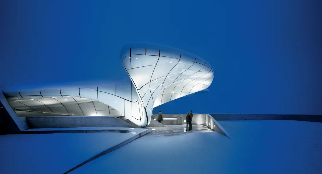 A modern glass building in front of a deep blue sky.