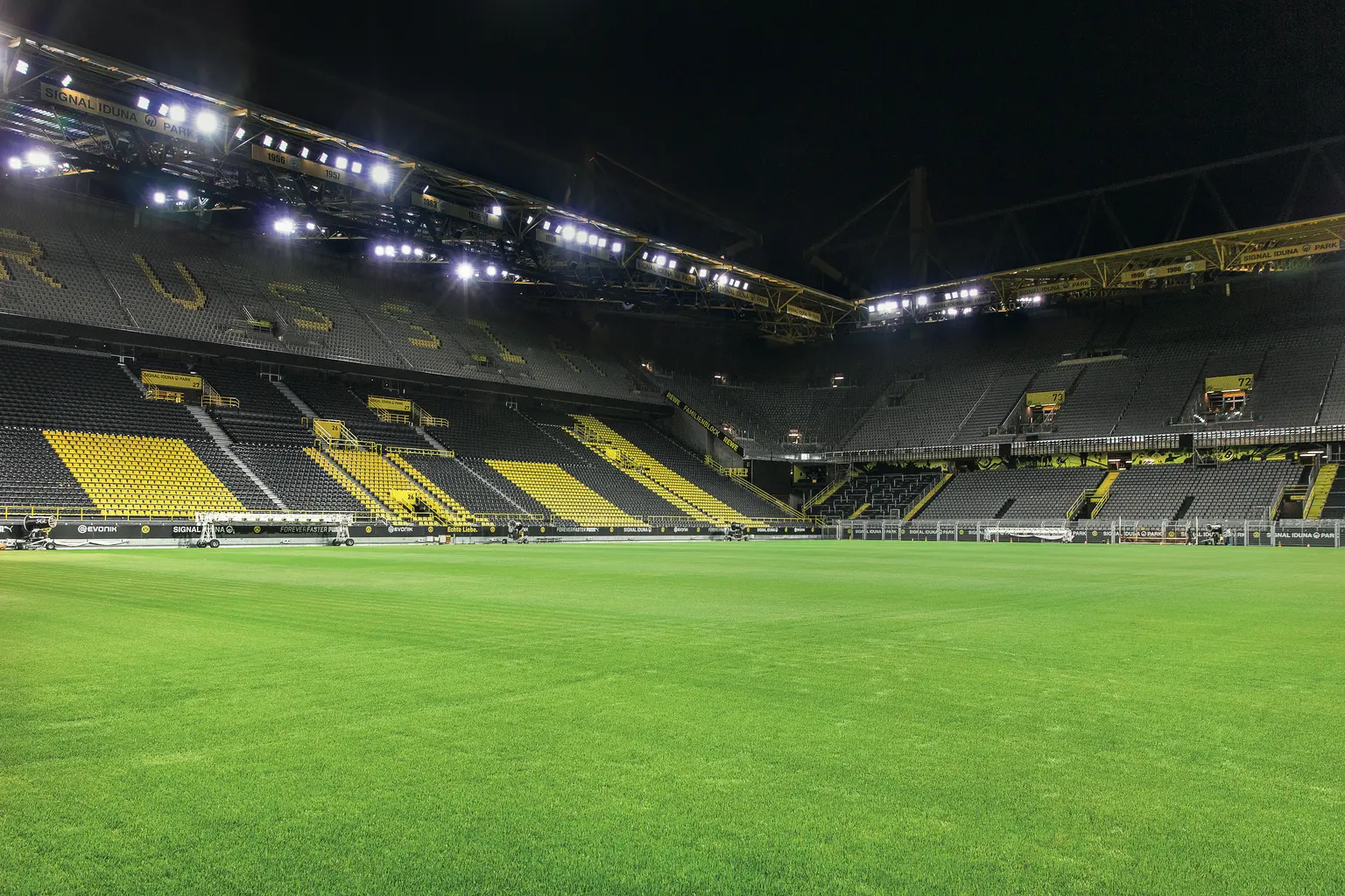 Eine Innenansicht des Signal Iduna Parks bei Nacht, die das hell erleuchtete grüne Spielfeld zeigt. Die ikonischen gelben und schwarzen Sitzbereiche und die beeindruckende Stahlkonstruktion des Stadions schaffen eine eindrucksvolle Atmosphäre.