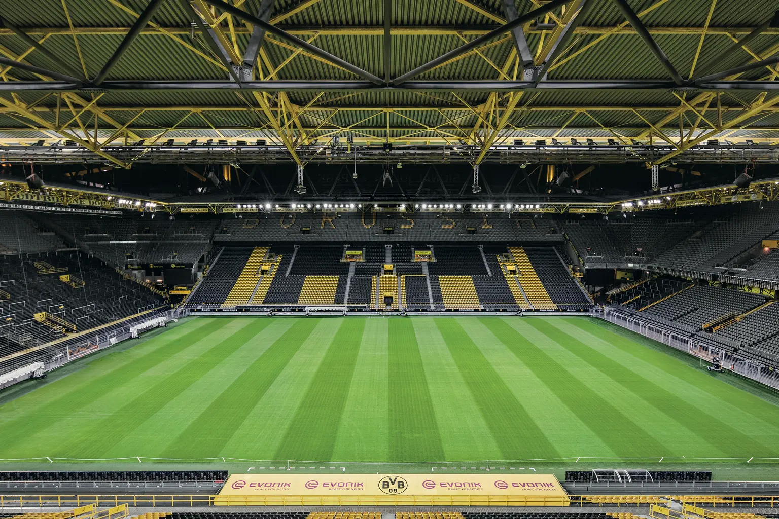 Eine Innenansicht des Signal Iduna Parks, die den lebhaften grünen Fußballplatz mit perfekt gemähten Streifen präsentiert. Die ikonischen gelben Stahlstrukturen und die gestuften Sitzplätze schaffen eine auffällige und moderne Stadionatmosphäre.