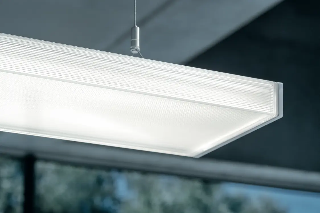 Die ECOOS LED-Pendelleuchte strahlt gleichmäßig helles Licht in einem modernen Raum mit großen Fenstern und sorgt für optimale Ausleuchtung.