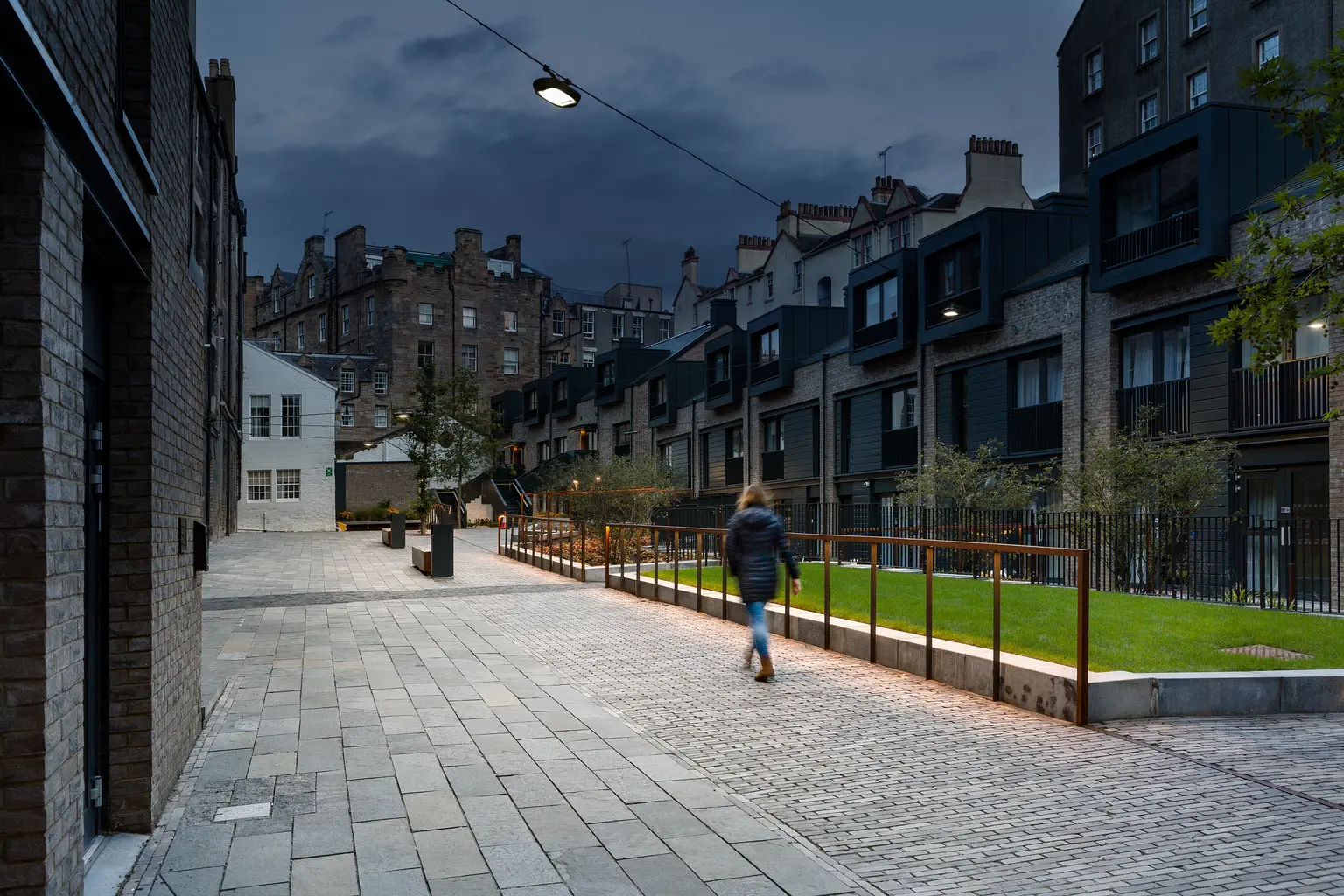 Modern luminaires provide uniform light along the walkway and green space, ensuring visibility and comfort for people passing through.