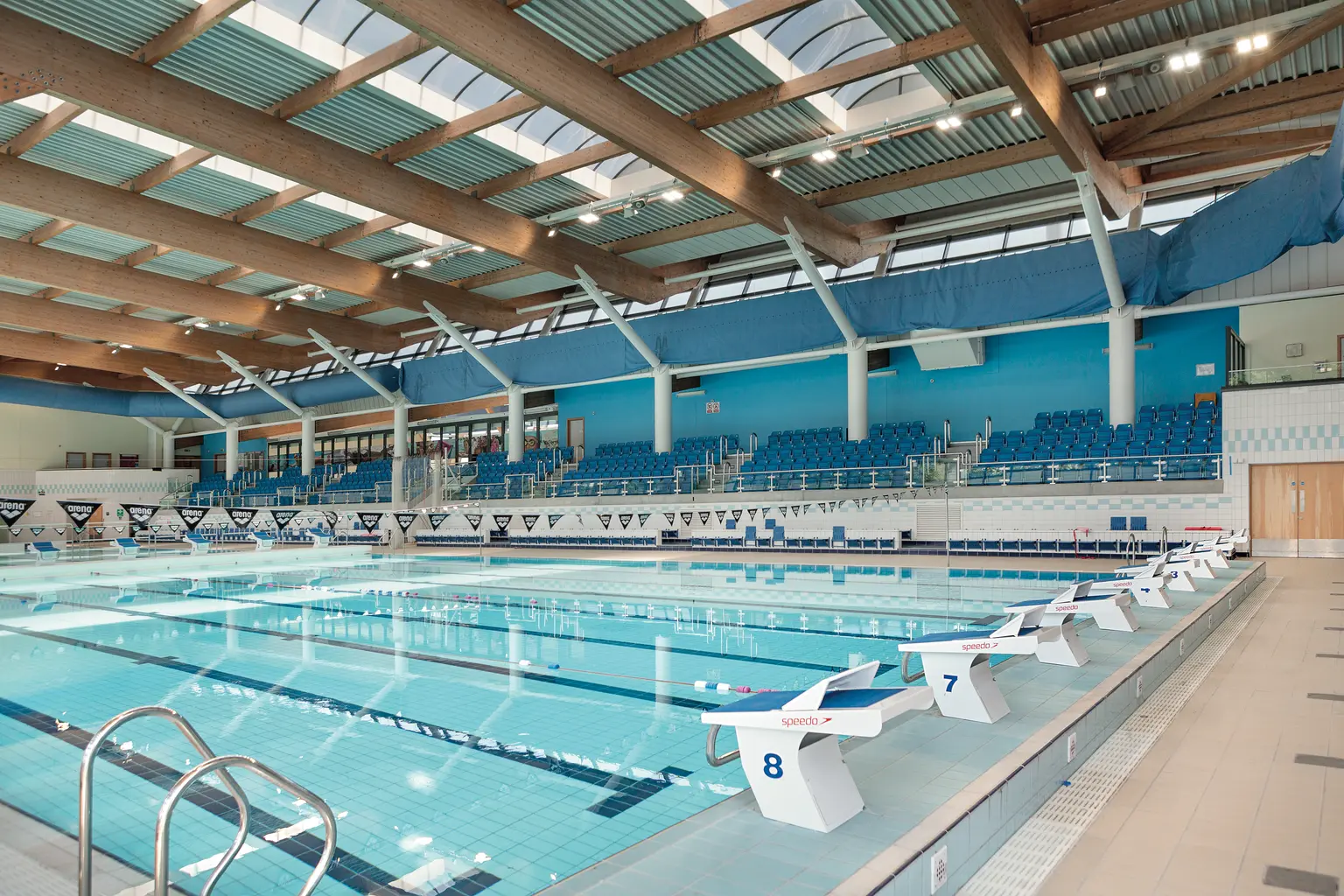 L'interno della piscina coperta del Liverpool Aquatics Centre è caratterizzato da corsie multiple con blocchi di partenza. Travi in legno, posti a sedere color azzurro e grandi finestre creano un'atmosfera luminosa e spaziosa.