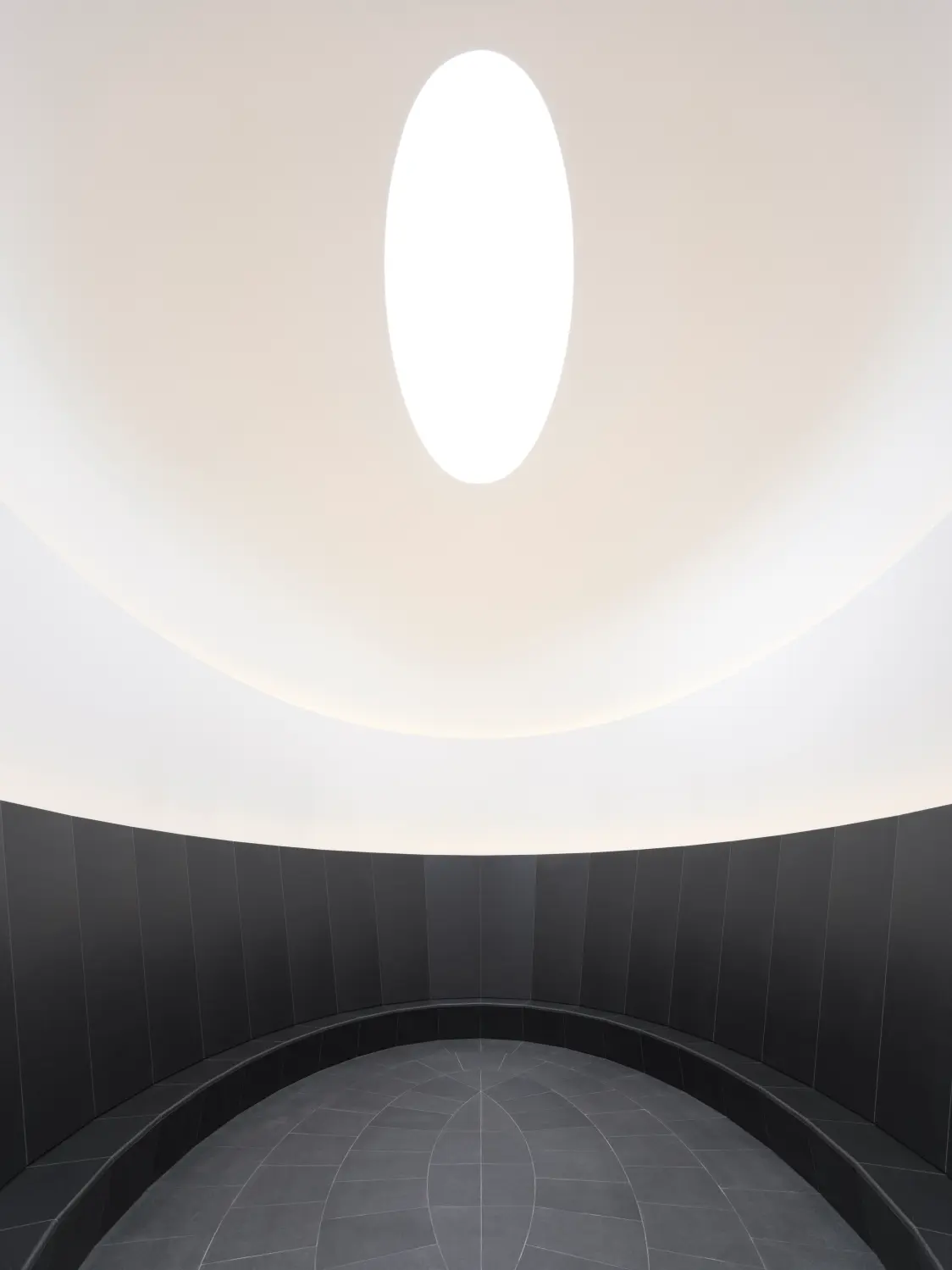 Binnenaanzicht van een Skyspace van James Turrell met een ovale lichtopening en zachte wit- en grijstinten die een minimalistische en meditatieve sfeer creëren.