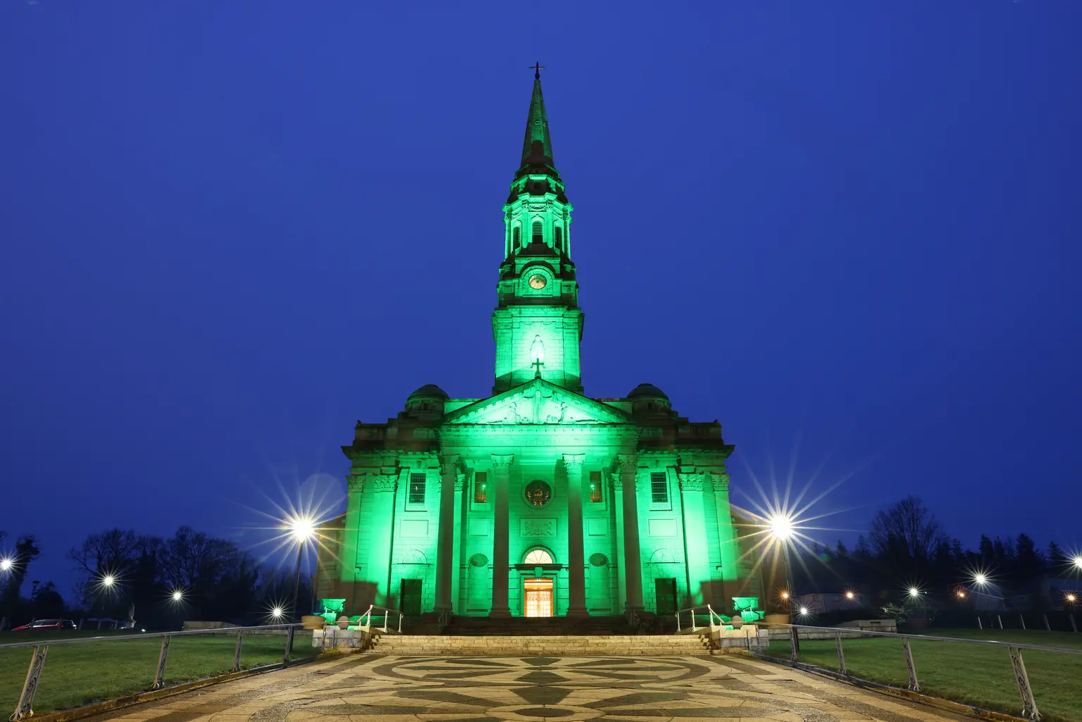 Ein monochromatisches grünes Lichtszenario verändert das Erscheinungsbild der Kirche, zeigt die Flexibilität der Beleuchtungslösung und betont die Präsenz des Gebäudes im städtischen Umfeld nach Einbruch der Dunkelheit.