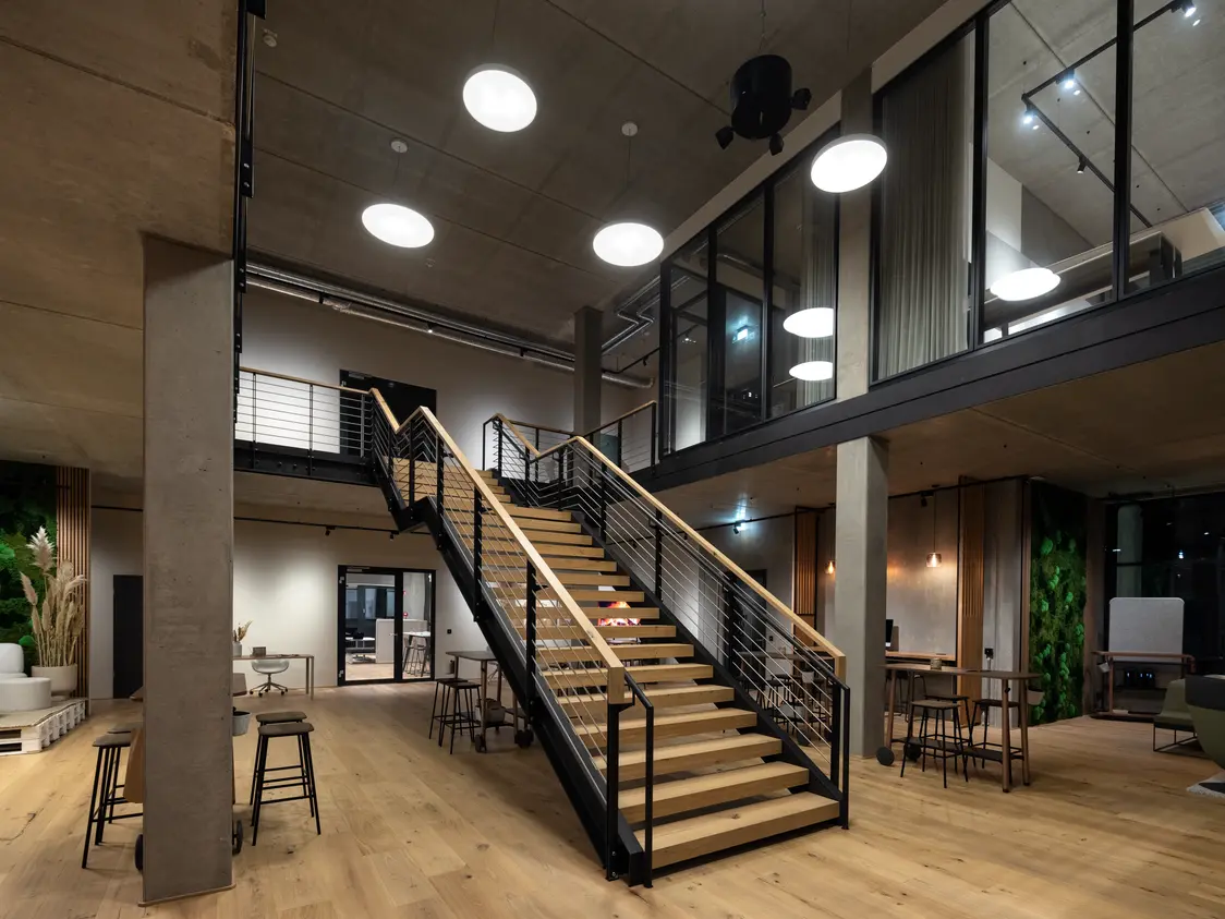 Modern entrance area of an office with an open wooden staircase and several round LED lights hanging from the ceiling for a pleasant atmosphere.