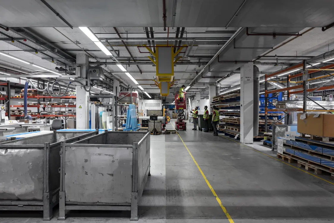 Produktionshalle mit Zumtobel Industriebeleuchtung, Maschinen und Arbeitern in reflektierendem Licht, Zumtobel