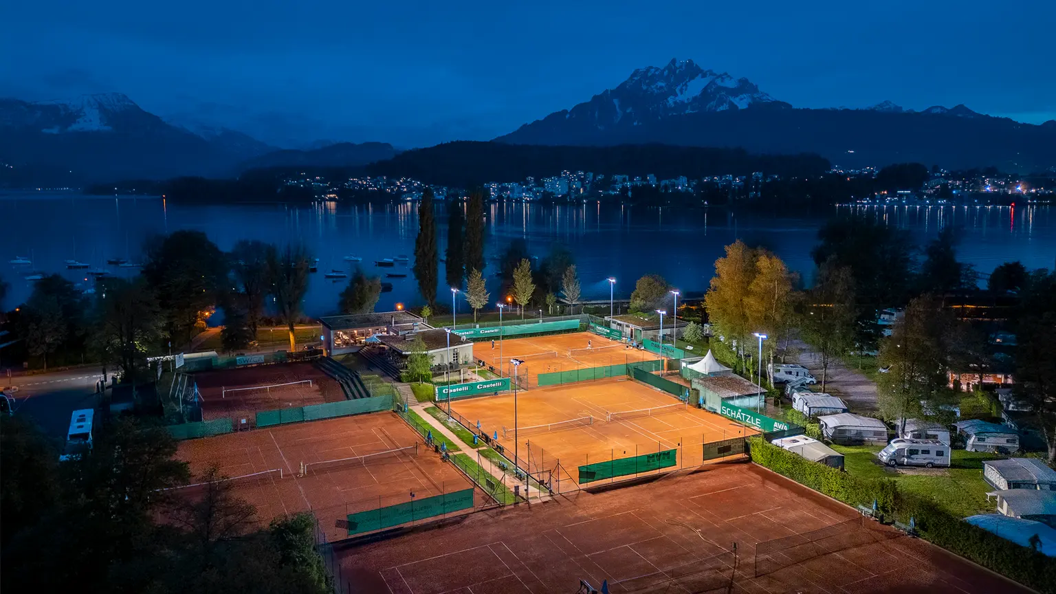 Un campo da tennis in lontananza con un solo campo illuminato grazie al comando della luce artificiale.