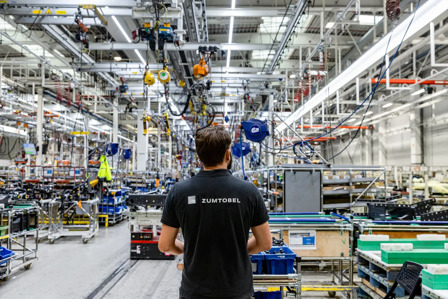 Un collaborateur de Zumtobel se tient dans un hall de production moderne, entouré de machines, de postes de travail et d’équipements industriels. La scène illustre l’environnement dynamique d’une entreprise technologique.