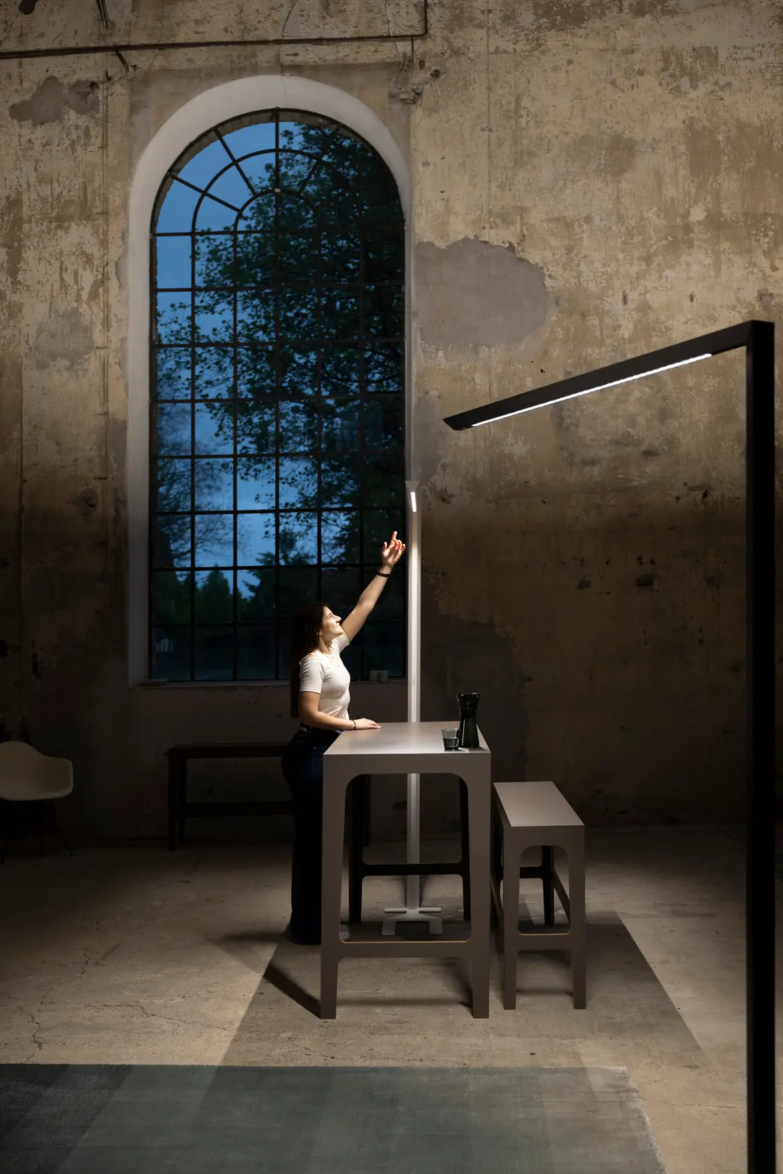 Eine Person und zwei Skena Tischleuchten in einem hohen industriellen Raum der durch die Leuchte einen modernen architektonischen Vibe bekommt. 