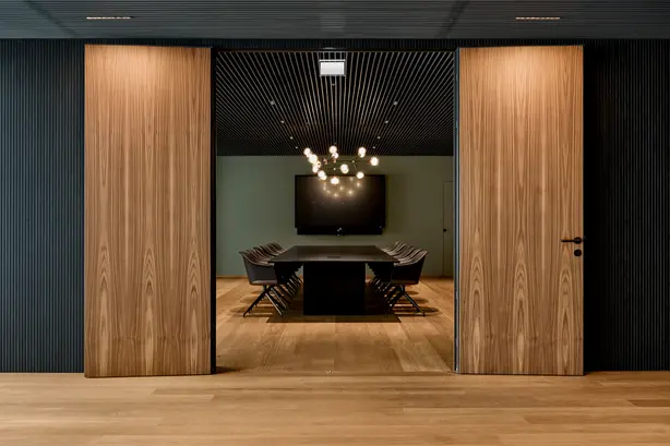 A modern office with clear lines and plenty of wood. A modern pendant luminaire from Zumtobel hangs in the centre.