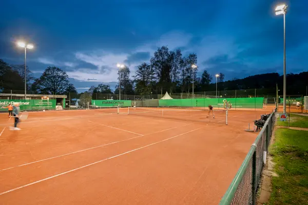 Campo da tennis illuminato di notte con giocatori di tennis mentre colpiscono