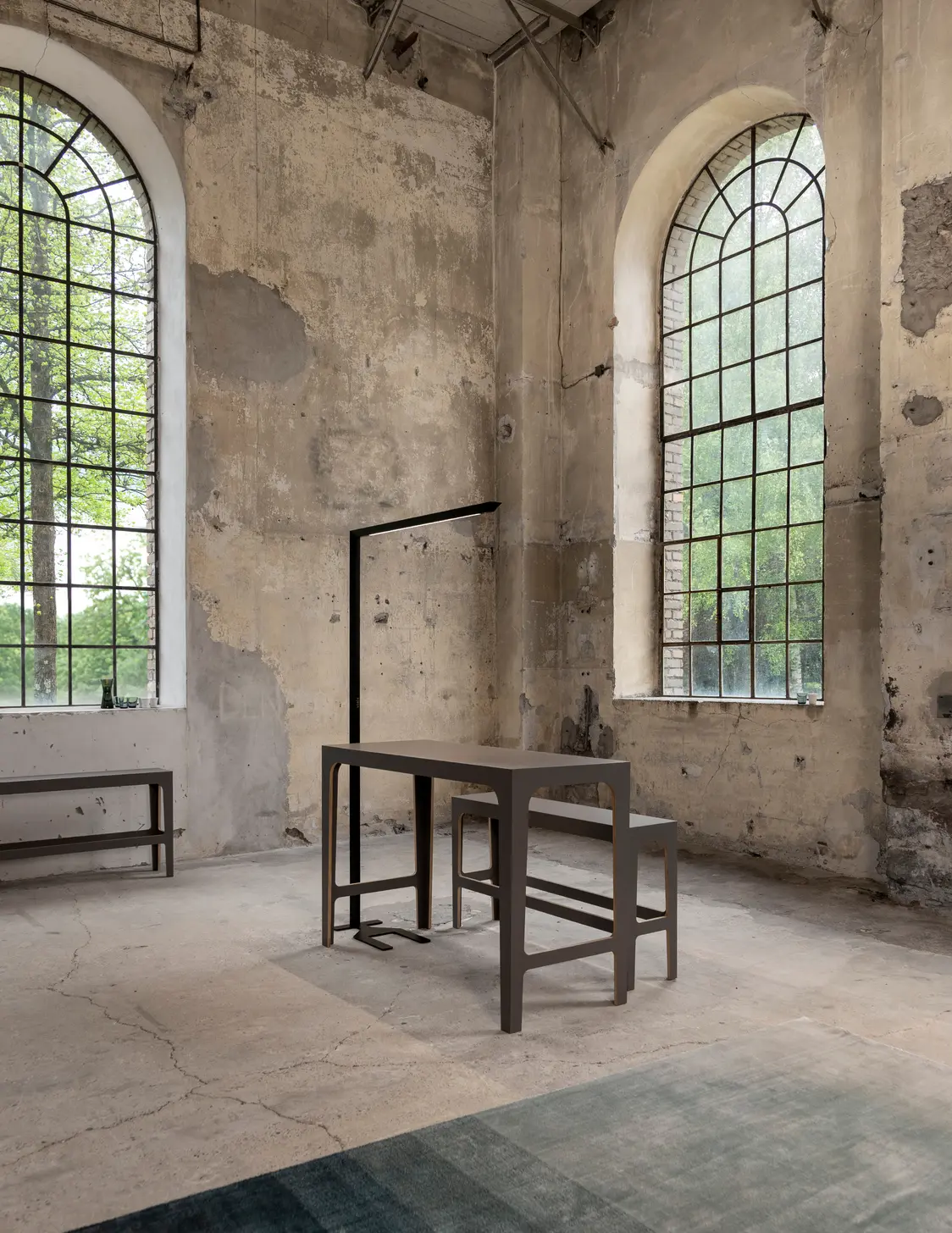 Die Skena Tischleuchte an einem Tisch. Im Hintergrund sind die hohen Fenster eines alten industriellen Raumes zu sehen.
