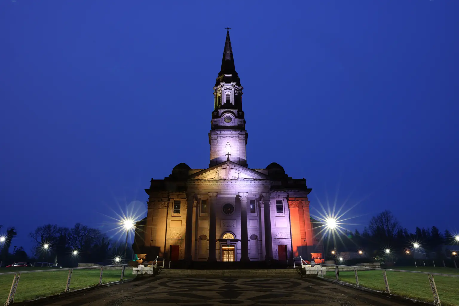 Dynamische Außenbeleuchtung taucht die Kirchenfassade in lebendige Farben, wodurch das Gebäude nachts zu einem markanten Wahrzeichen wird und je nach Anlass unterschiedliche Lichtstimmungen ermöglicht.
