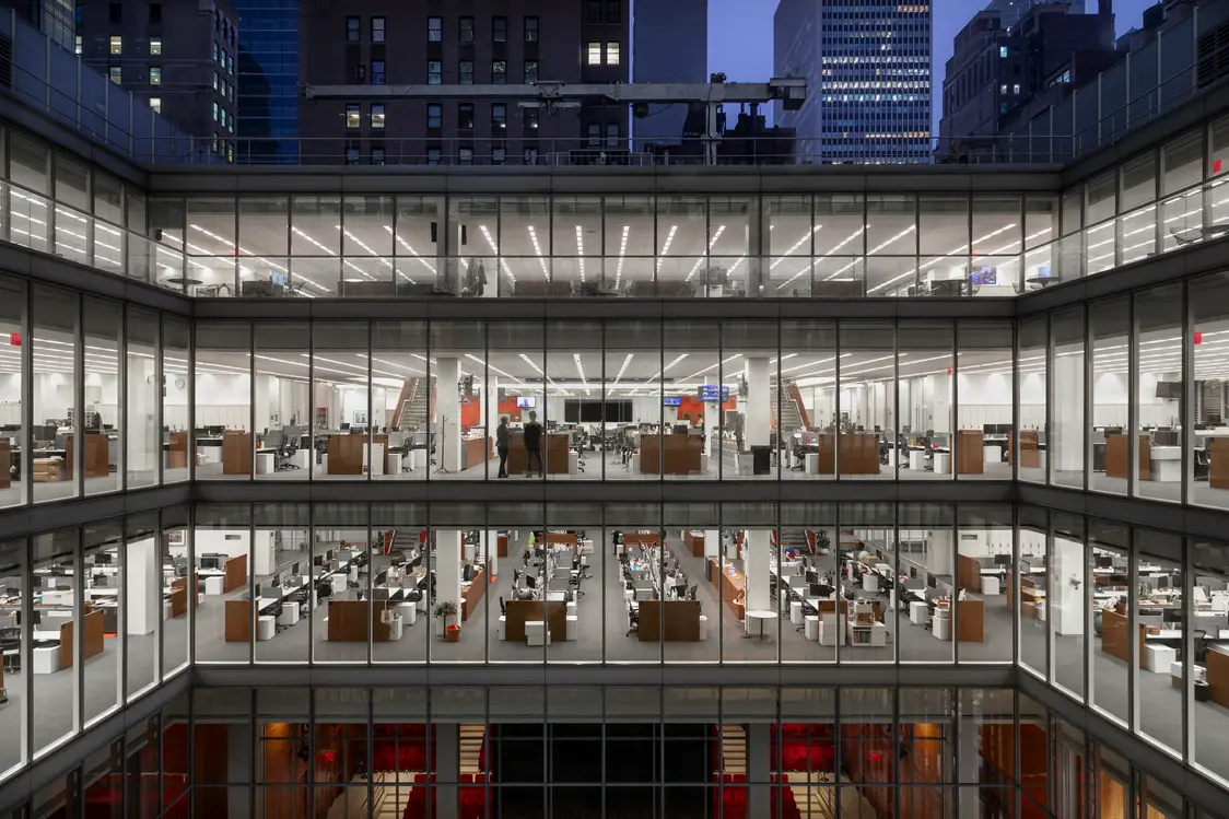 Un moderno edificio per uffici con grandi facciate in vetro, che mostra diversi piani di spazi di lavoro open space con scrivanie e illuminazione notturna. La struttura offre una visione di un ambiente di lavoro produttivo e organizzato.
