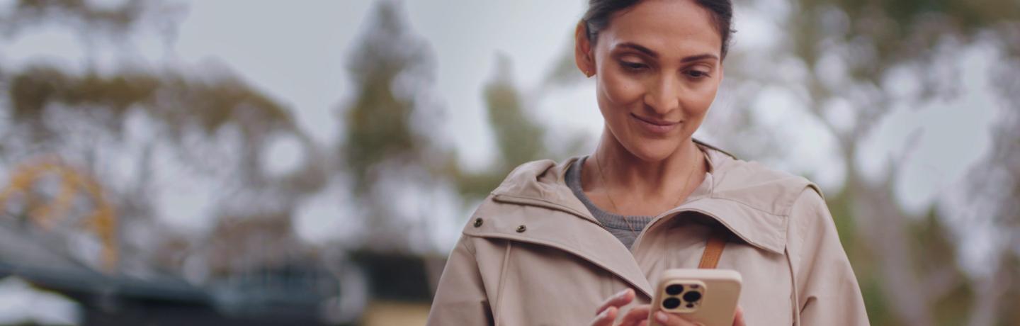 Smiling woman using a smartphone outdoors.