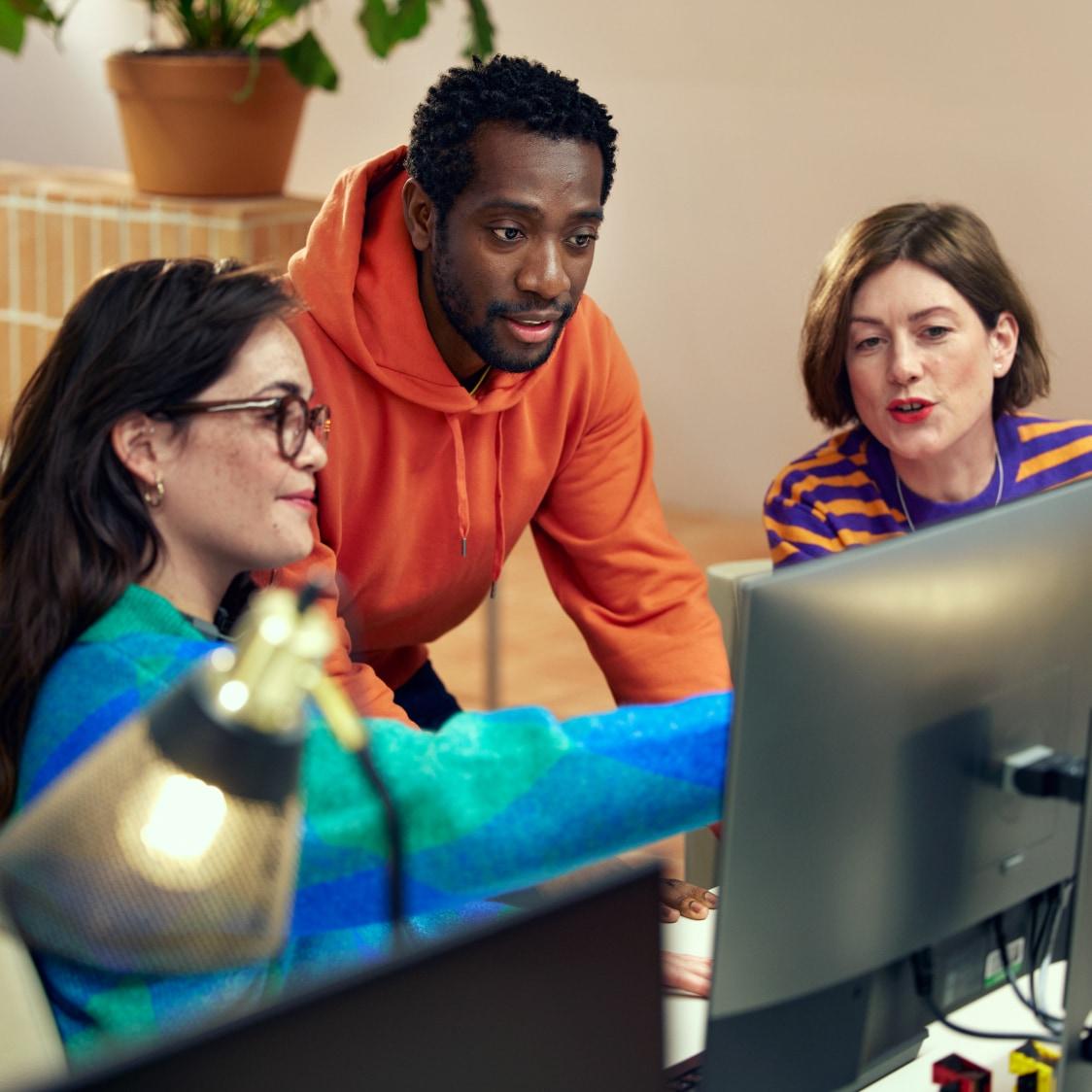 Tres colegas colaborando sobre una pantalla de computadora en un entorno de oficina.