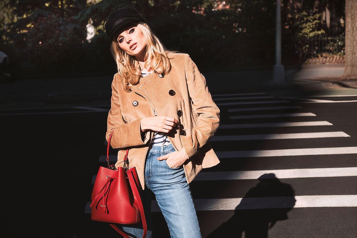 Frau in einer braunen Jacke und schwarzem Hut mit roter Handtasche auf einem Fußgängerübergang