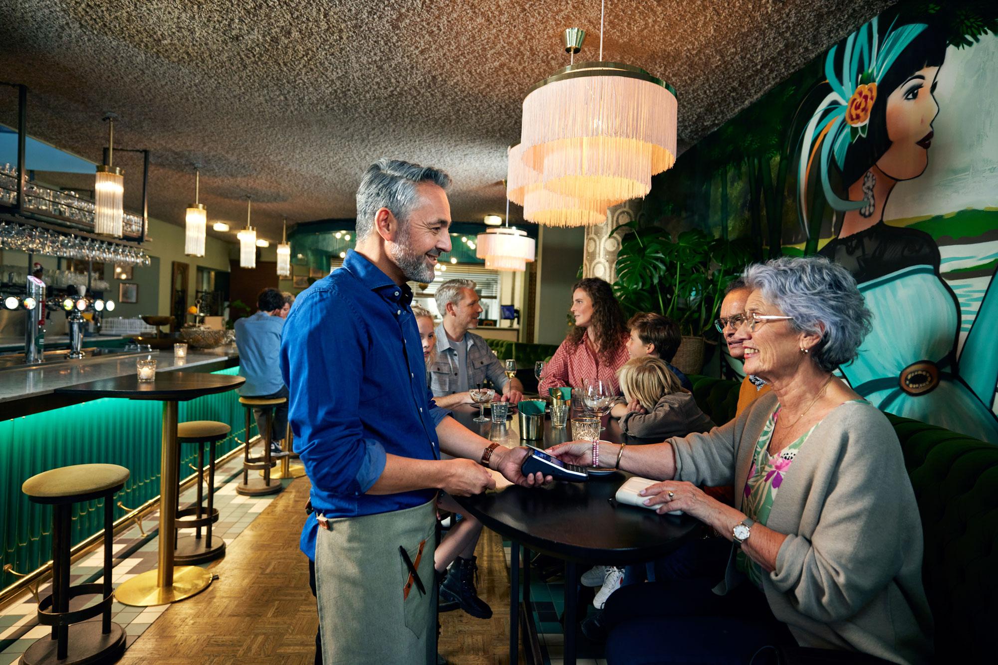 En kvinde i en restaurant betaler ved at tappe sin kort på Adyens V400m-terminal.
