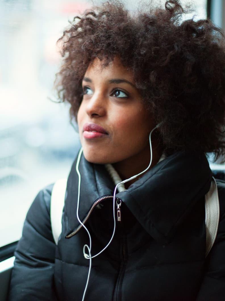 Woman with curly hair wearing earphones and looking away thoughtfully.