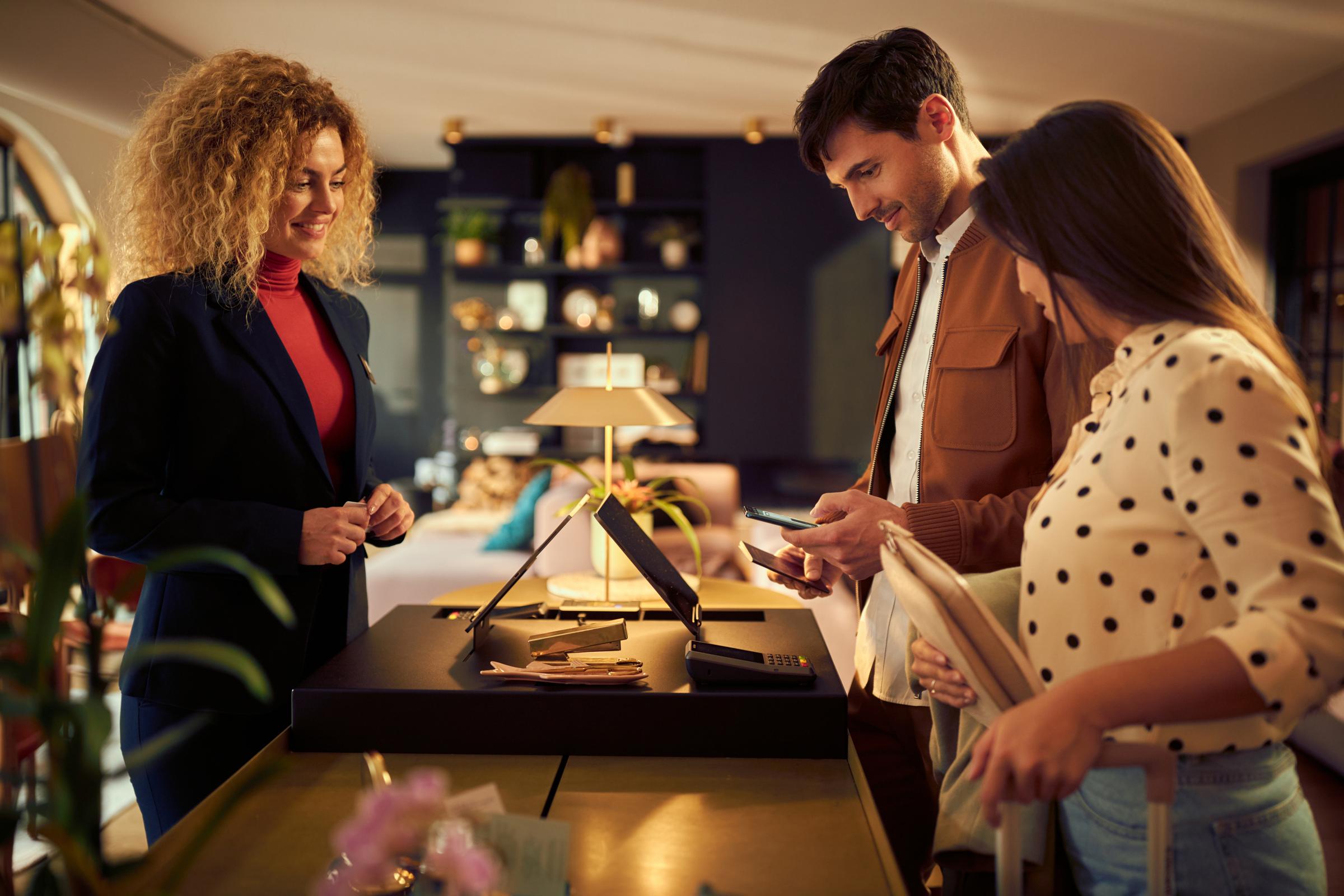Kunder som betalar med telefon vid en detaljhandelskassa med en leende anställd