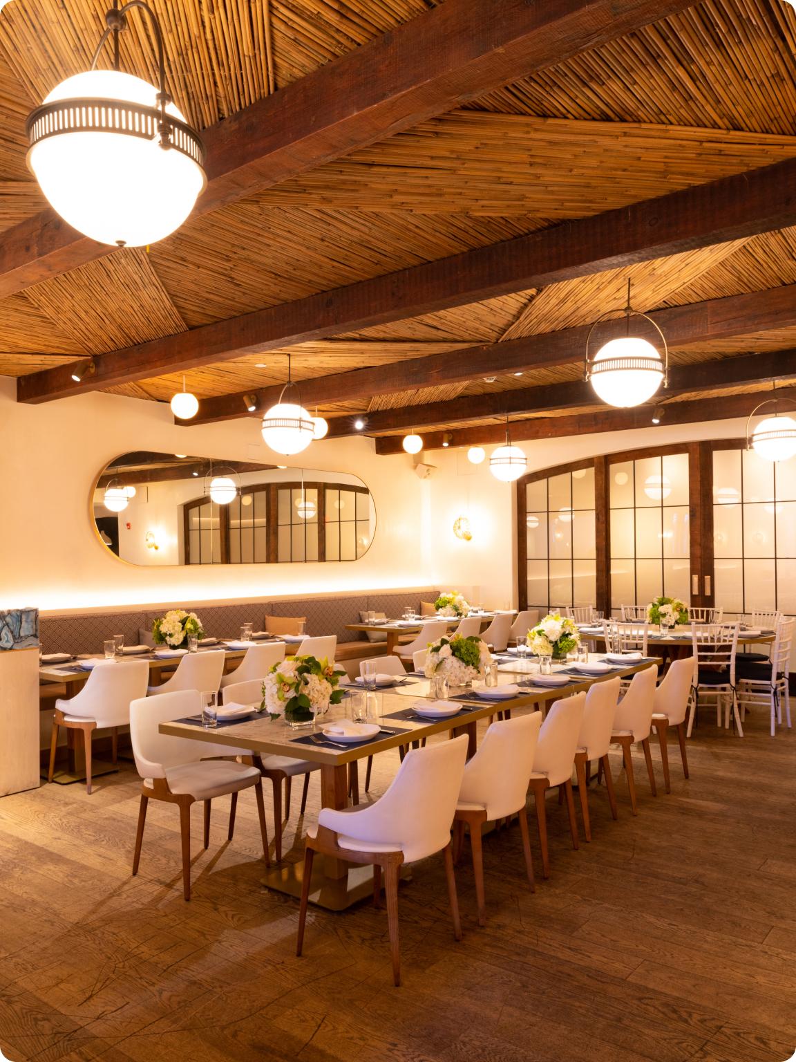 Elegant restaurant interior with wooden tables, white chairs, and warm lighting.